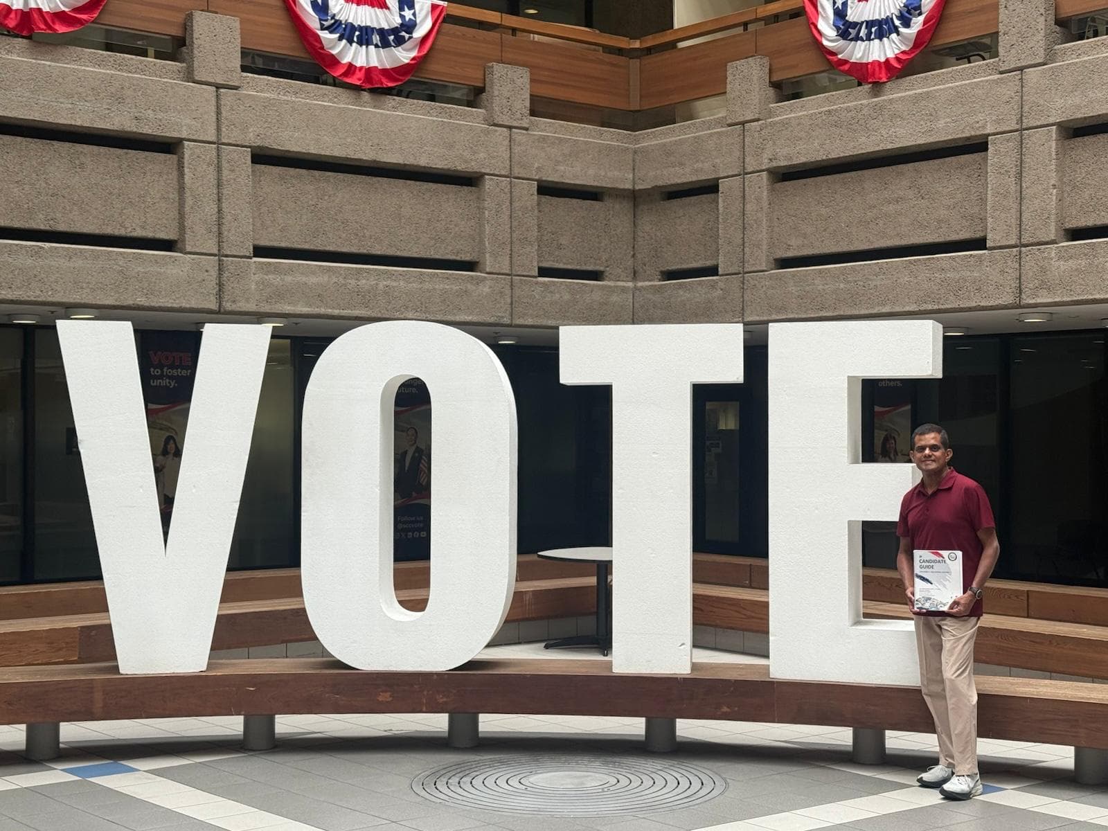 Sundar Subbarayan standing beside a giant VOTE sign, holding his official candidate guide